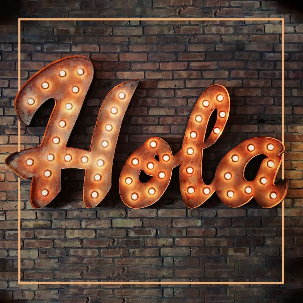 Light up sign against a brick wall that says hola
