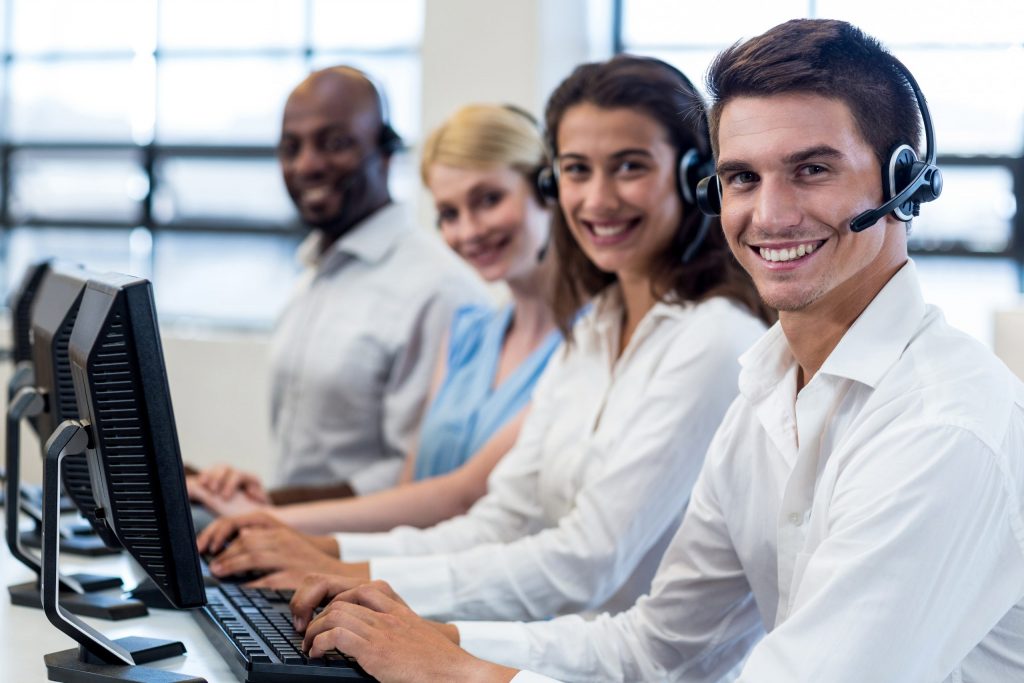 group of coworkers smiling at camera while answering calls on their computers